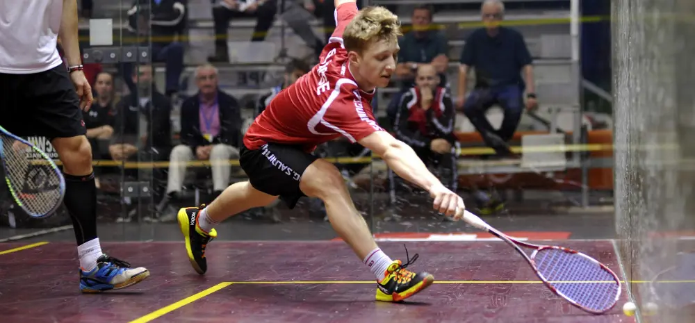 A professional squash player reaching for a difficult shot